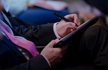 Person in suit sitting down at conference takes notes