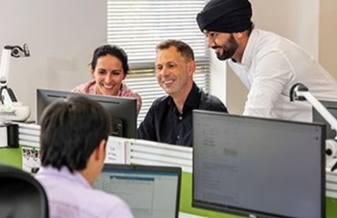 Man with black turban stands next to two colleagues looking at computer screen