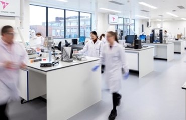 Scientists wearing white lab-coats walk around an RB laboratory