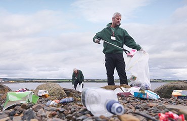 Two volunteers picking up plastic waste on a beach 