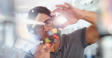 Scientist wearing glasses holds up coloured cubes to analyse them with light shining from behind