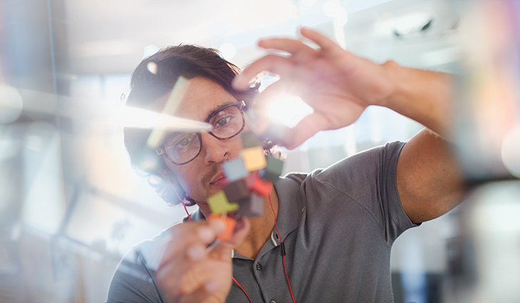 Scientist wearing glasses holds up coloured cubes to analyse them with light shining from behind