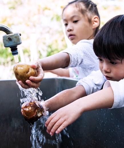 Children are washing raw vegetable in the outside kitchen.