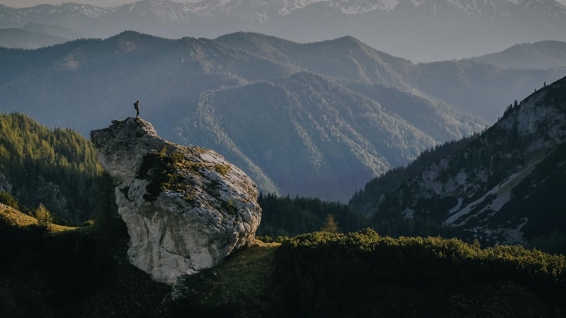 Person on a cliff looking off in to the distance, the fore-ground, of the forest and the mountains in the distance.