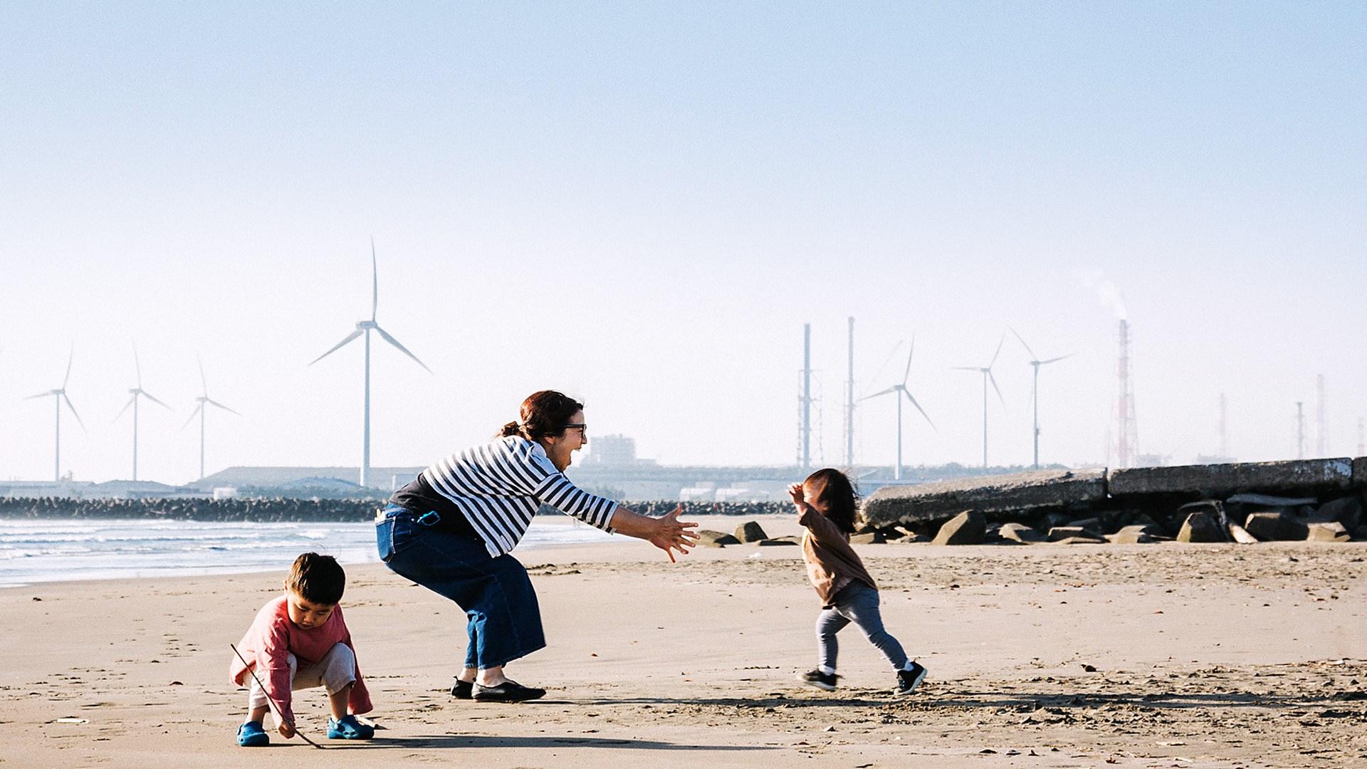 Family relaxed on the beach close to wind farm.