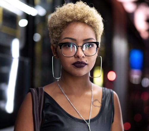 Woman in glasses looks into the camera with city lights behind her
