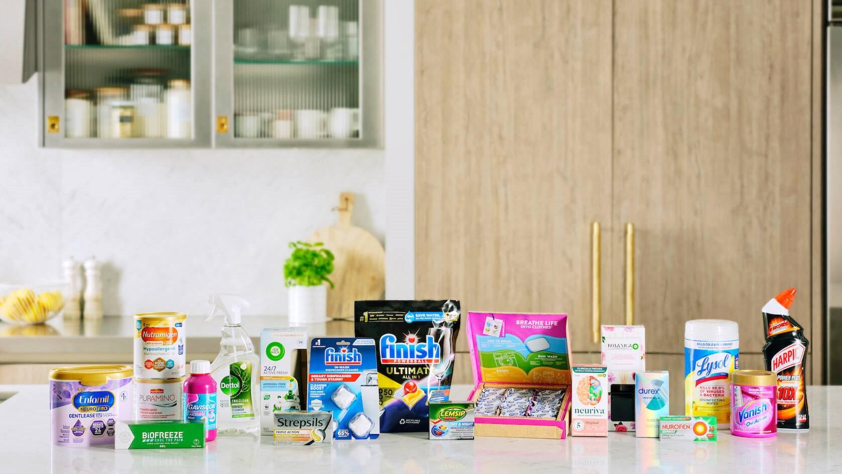 A lineup of products from the Reckitt range of brands lined up on a kitchen bench. Includes products from Finish, Harpic, Vanish, and Lysol.