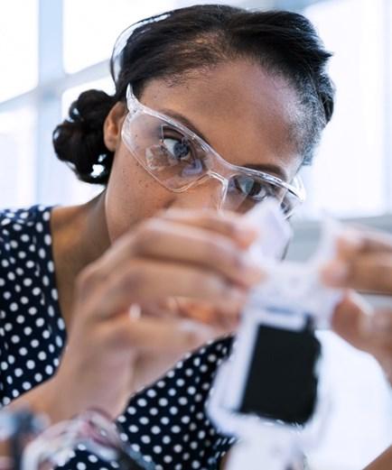 Lady wearing protective glasses looking at the mechanism of her project