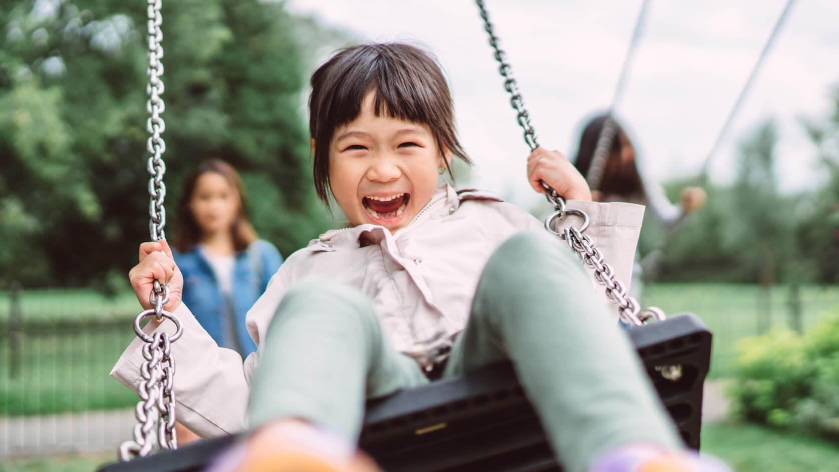 A child laughs while being pushed by her mother on a swing